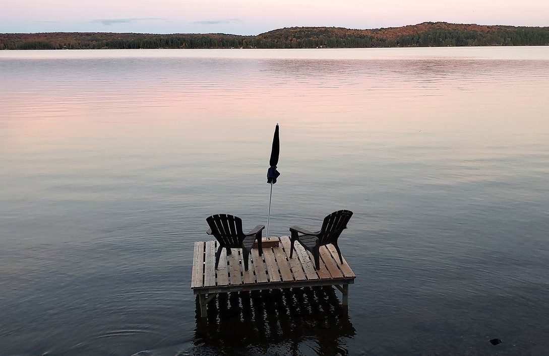 Muskoka chairs sit on a dock looking over Boshkung Lake, in Algonquin Highlands