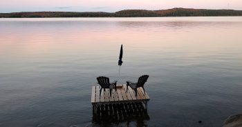 Muskoka chairs sit on a dock looking over Boshkung Lake, in Algonquin Highlands