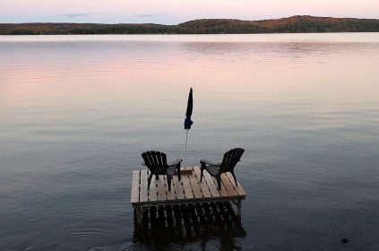 Muskoka chairs sit on a dock looking over Boshkung Lake, in Algonquin Highlands